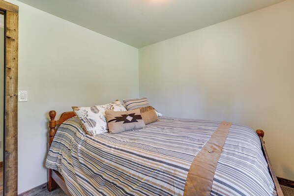 A neatly made bed with striped bedding and a wooden headboard, positioned against a plain wall.