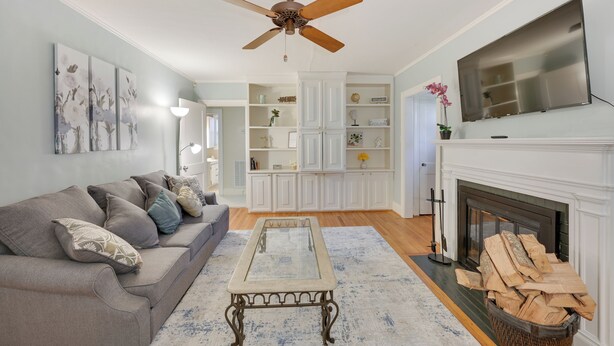 A living room with a grey sofa, a glass coffee table, a fireplace, and a ceiling fan. - Quaint Goldsboro Home w/ Screened-in Porch! (Goldsboro)
