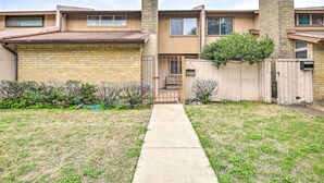 A two-story residential building with a brick facade, a wooden fence, and a concrete pathway leading to the entrance.