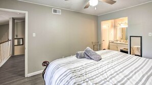 A bedroom with a bed, a ceiling fan, a bathroom with a sink and mirror, and a hallway leading to another room.