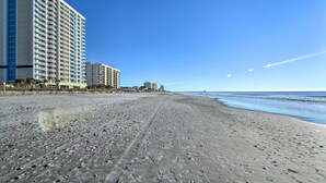 Una playa con huellas, un edificio de gran altura y un cielo azul despejado.