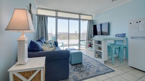 Un salón con sofá, televisor, ventilador de techo y vista al exterior.
