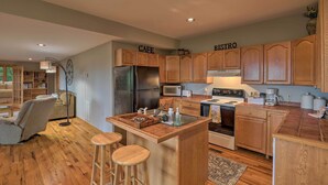 A kitchen with wooden cabinets, a central island with stools, a refrigerator, stove, and microwave. - Black Mountain Gem w/ Inviting Deck & Scenic Views (Black Mountain)