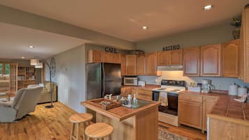 Une cuisine avec des meubles de rangement en bois, un îlot central doté de tabourets, un réfrigérateur, une cuisinière et un four à micro-ondes.