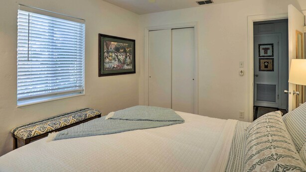 A bedroom with a bed, a bench, a ceiling fan, a window with blinds, and a door. - Florida Home ~ 10 Mi to St Pete Beach! (St. Petersburg)