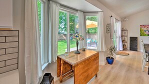 Een kamer met een houten bureau, een bloempot en een groot raam met gordijnen.