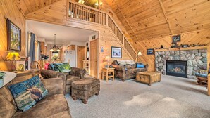 A cozy log cabin interior with a stone fireplace, wooden furniture, and a staircase leading to an upper level.