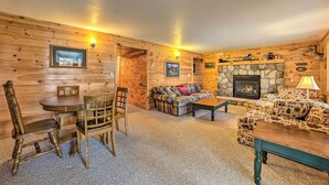 A cozy log cabin interior with a stone fireplace, wooden furniture, and a dining area.