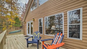 A wooden deck with Adirondack chairs, large windows, and a view of autumn trees.