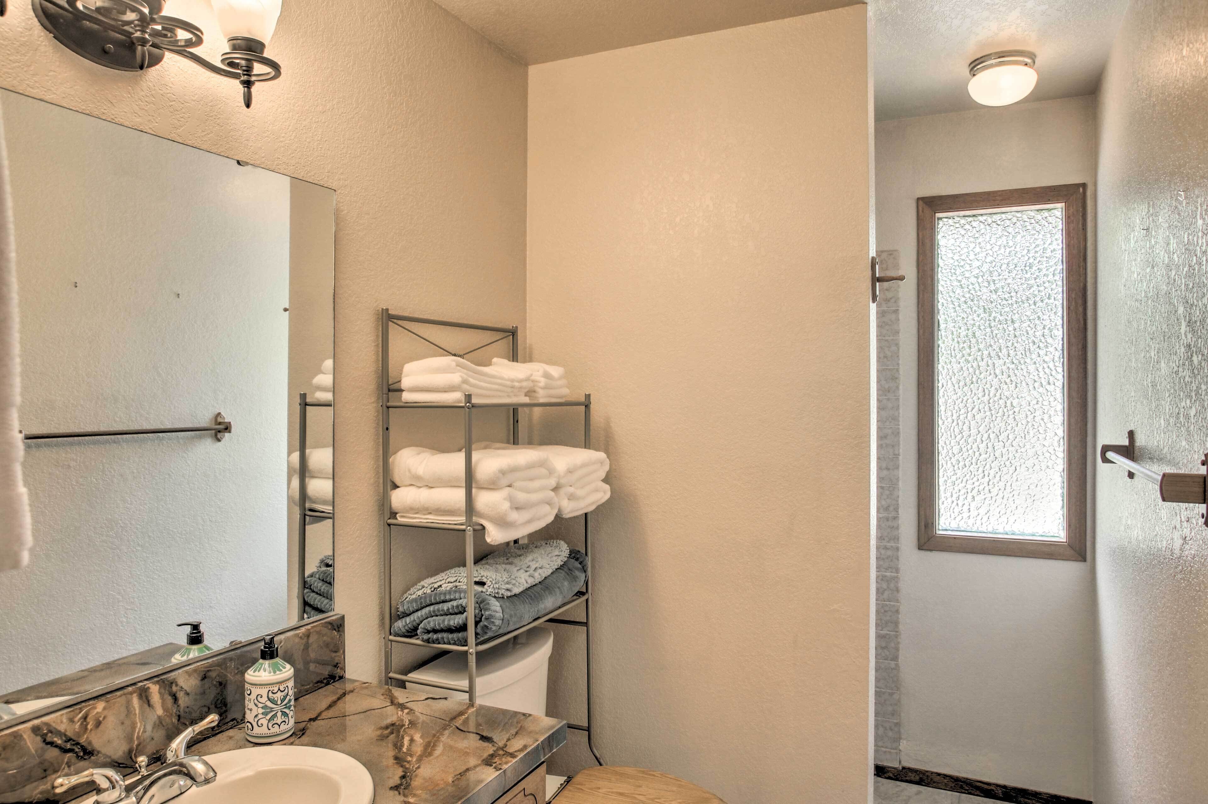 Une salle de bain avec un lavabo en marbre, un grand miroir, un porte-serviettes avec des serviettes pliées, un espace douche et une porte en verre dépoli.