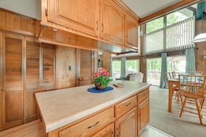 A kitchen with wooden cabinets, a central island with a blue placemat, and a dining area with a table and chairs. - Cozy Dover Home w/ Boat Dock, Fire Pit & Deck! (Dover)