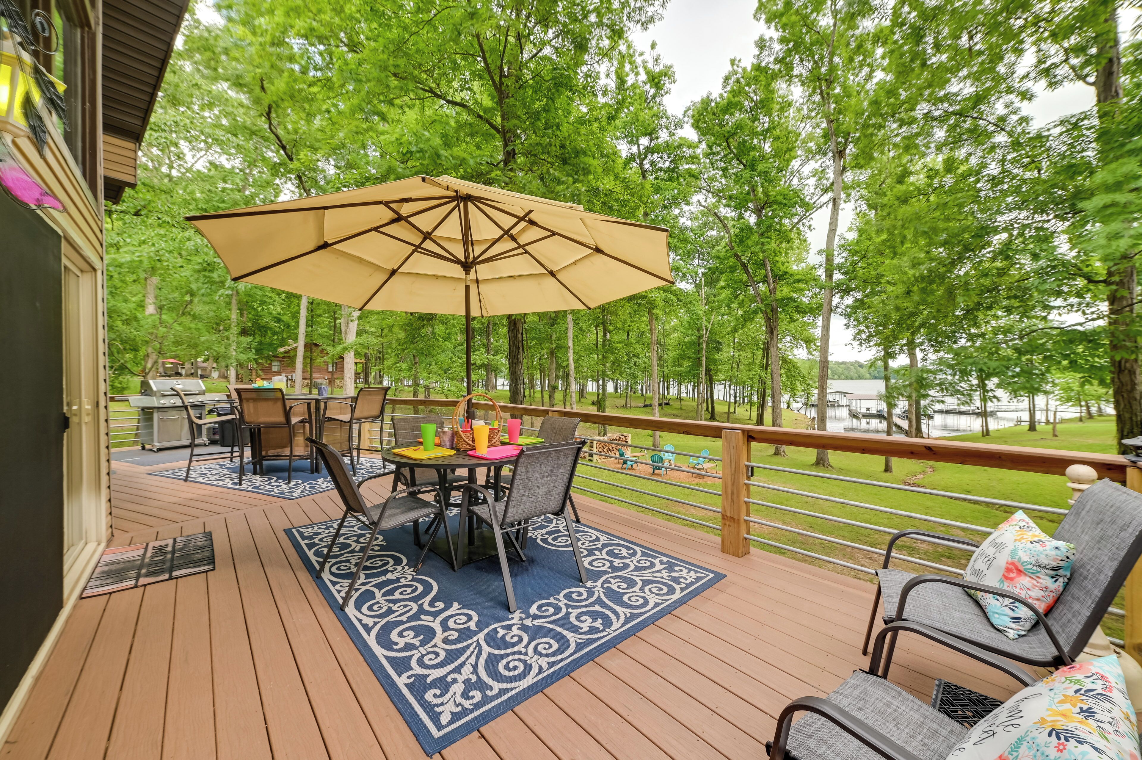 A wooden deck with a table and chairs, an umbrella, and a view of a lake surrounded by trees.
