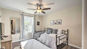 A bedroom with a bed, a ceiling fan, a window with curtains, and a bedside table.