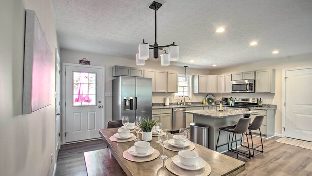 A modern kitchen with white cabinets, a central island with bar stools, a stainless steel refrigerator, and a microwave.