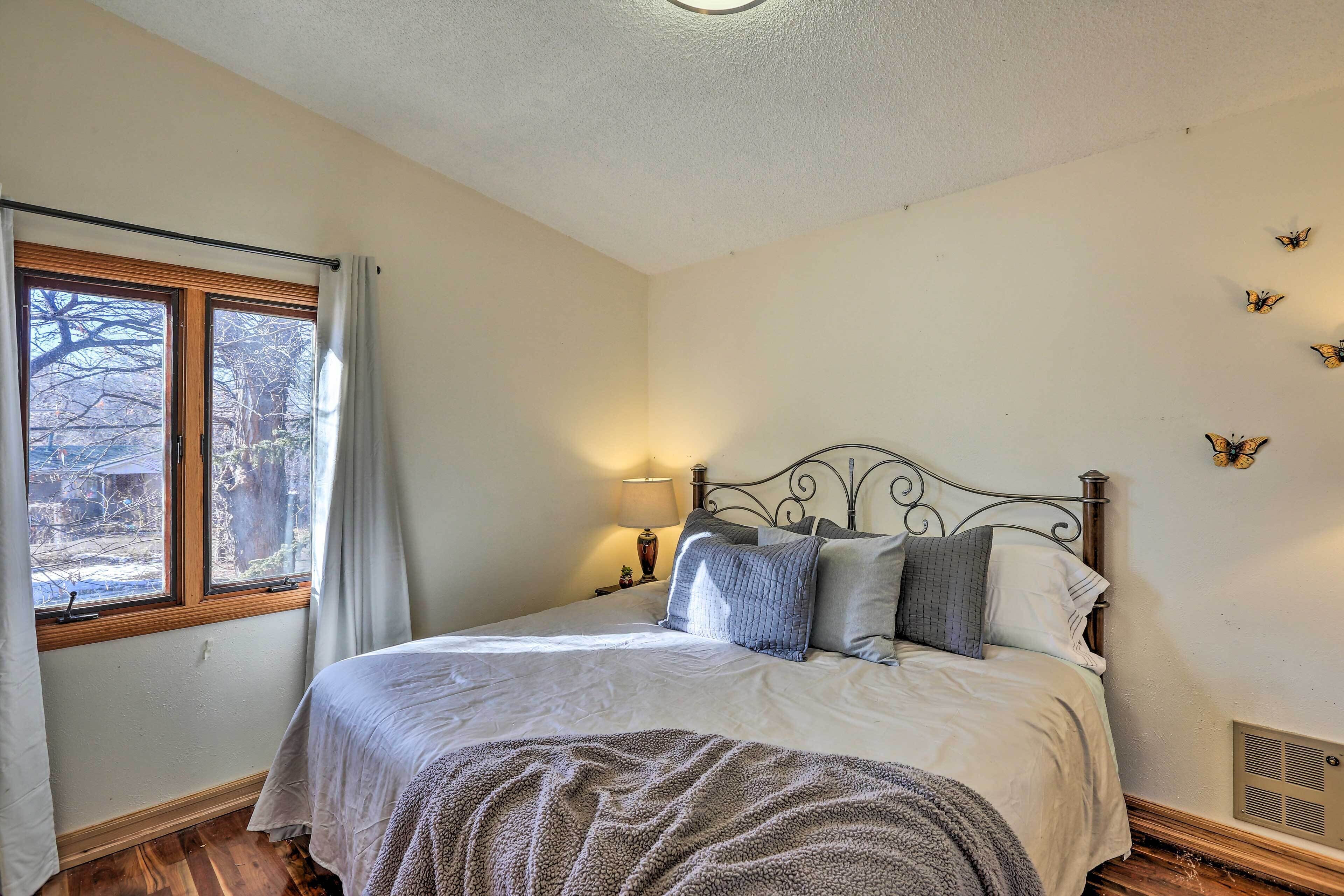 Quarto com cama, janela com cortinas, luminária na parede e decoração com borboletas.