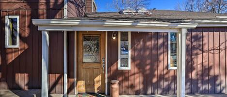 A wooden house with a porch, a front door, and a small window.