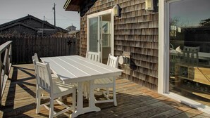 A wooden deck with a white table and chairs, a sliding glass door, and a view of a building in the background. - Walk to Ocean! Chic 'summer House Cottage' (Pacific Beach)