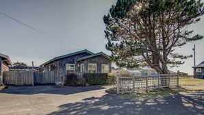 A two-story wooden house with a fenced driveway and a large pine tree in front. - Walk to Ocean! Chic 'summer House Cottage' (Pacific Beach)