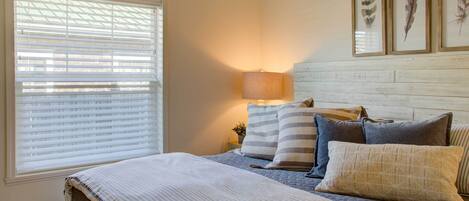 A bedroom with a bed, pillows, a bedside lamp, and framed feather art on the wall.