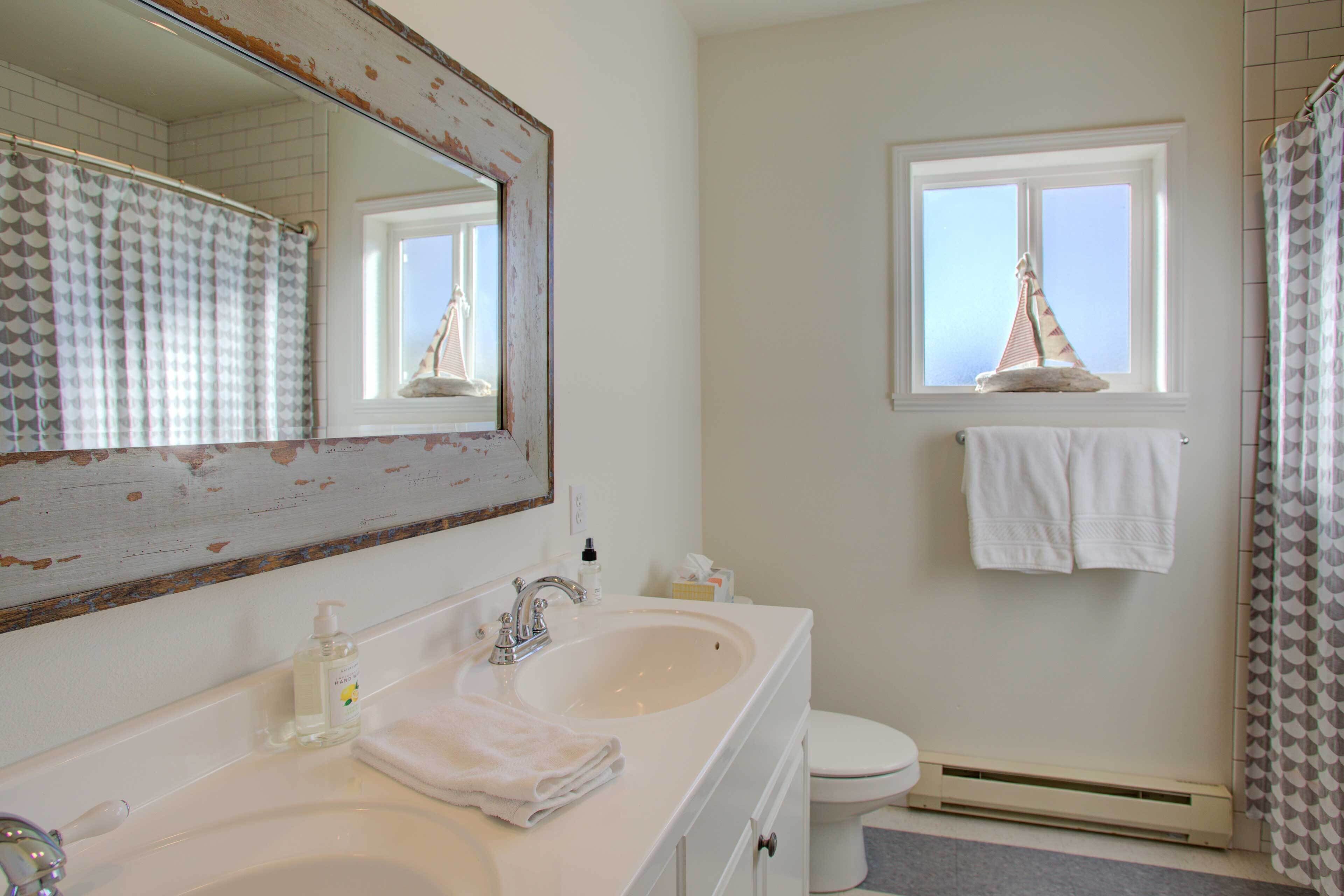 A bathroom with a white sink, a mirror, a towel rack, and a window with a sailboat decoration.