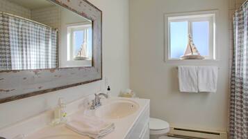 A bathroom with a white sink, a mirror, a towel rack, and a window with a sailboat decoration.
