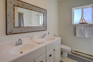 A bathroom with two sinks, a toilet, a large mirror, and a window with a towel rack.