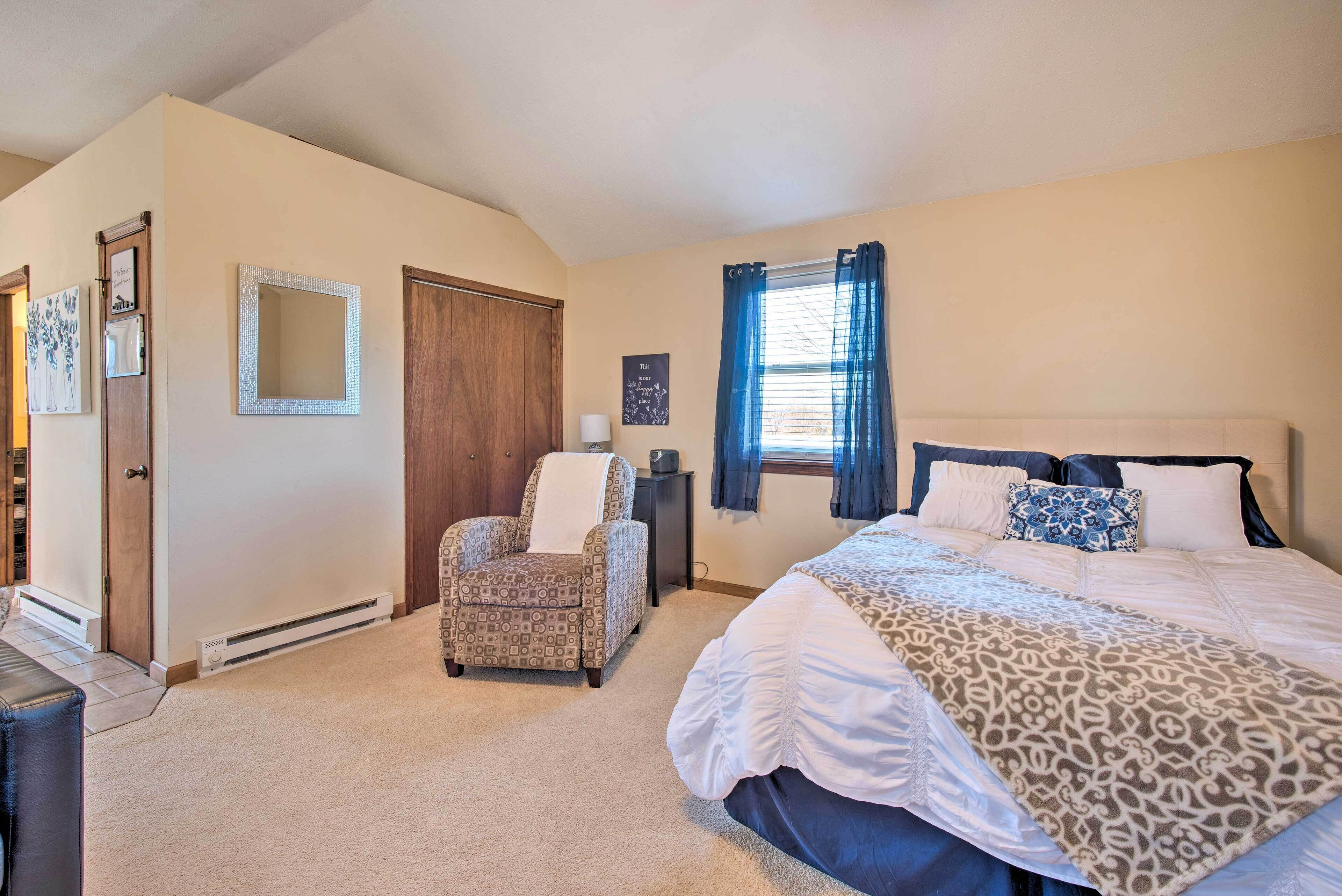 A bedroom with a bed, a chair, a desk, and a window with curtains.