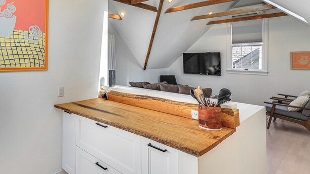 A kitchen with a wooden countertop, white cabinets, and a loft bedroom with exposed beams. - Steps to NYC Train! Charming Carriage House Loft (Glen Ridge)
