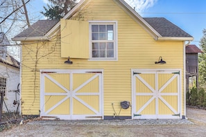 A yellow house with two garage doors, a window, and a small shed in the background.