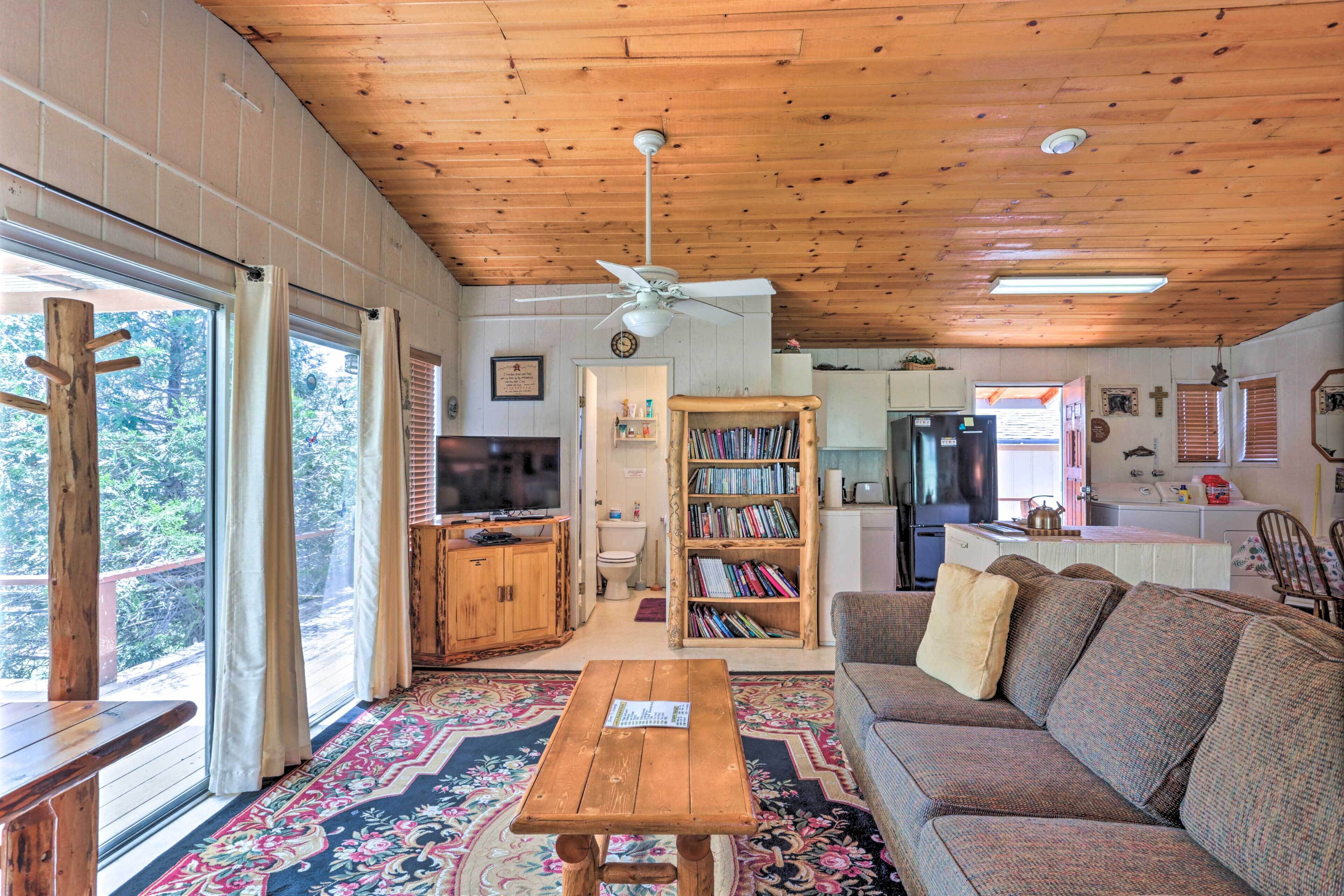 A cozy cabin interior with a wooden ceiling, a large bookshelf, a sofa, and a dining area.