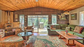 A cozy living room with a wooden ceiling, a green sofa, a wooden coffee table, and a large window overlooking a garden. - Gorgeous Oakhurst Retreat w/ Swimming Hole! (Oakhurst)