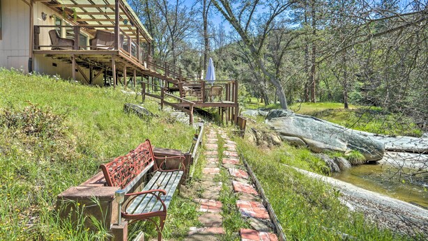 A wooden deck with outdoor seating and a stone pathway leading to a building. - Gorgeous Oakhurst Retreat w/ Swimming Hole! (Oakhurst)