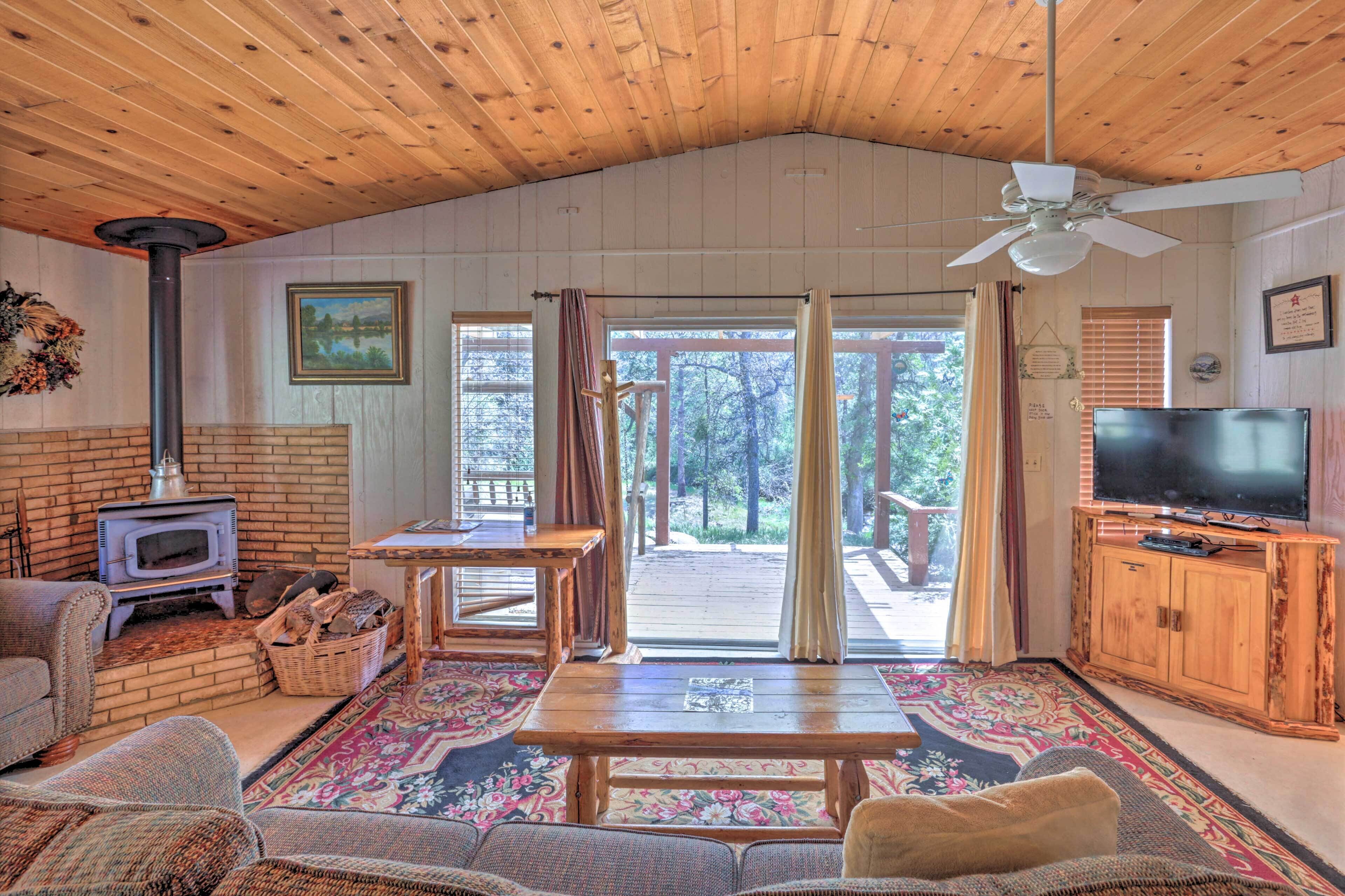 A cozy cabin interior with a fireplace, wooden furniture, a television, and a large window offering a view of the outdoors.