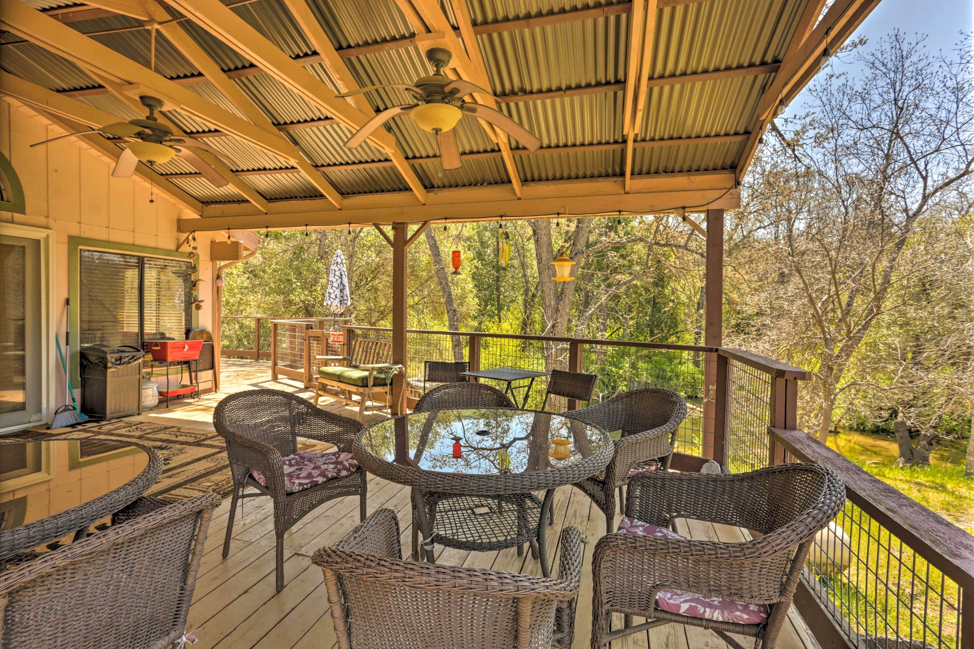 A covered outdoor deck with wicker furniture, a glass table, and a ceiling fan.