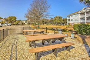 A park area with picnic tables, a pond, and a building with balconies. - Resort Condo w/ Balcony & Pool Access! (North Myrtle Beach)