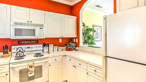 Una cocina con armarios blancos, microondas, estufa y refrigerador. Hay un letrero en la pared que dice 