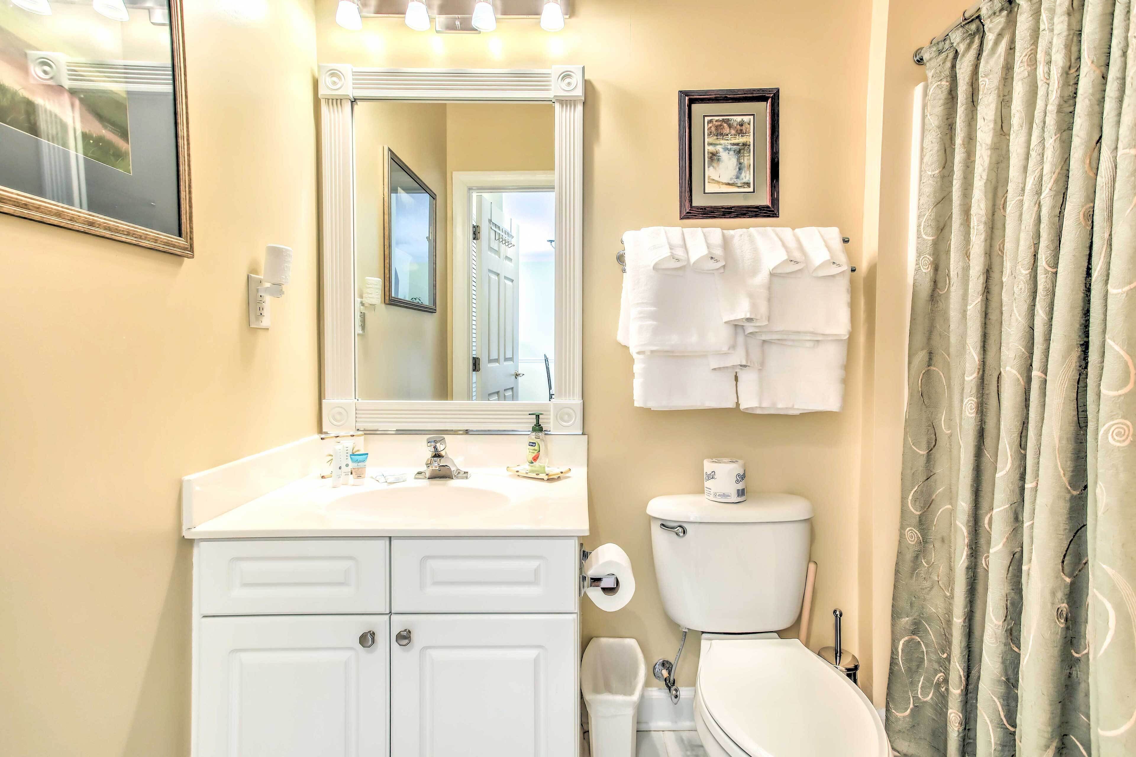A bathroom with a white sink, mirror, toilet, and shower curtain.
