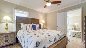 A bedroom with a bed, nightstands, a ceiling fan, a door, and a window. - Charming Gulfport Home ~ 2 Mi to Marina (Gulfport)