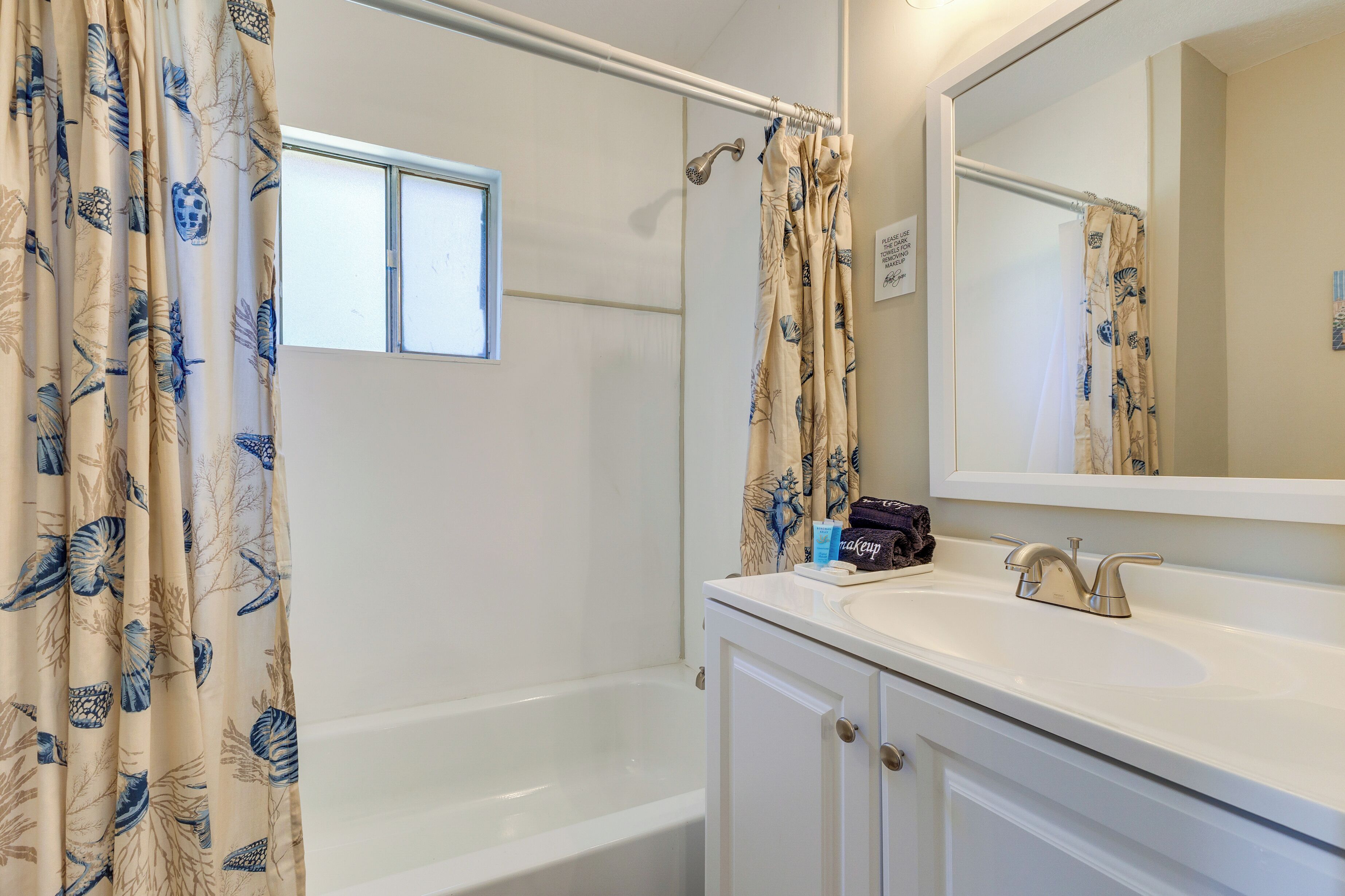 A bathroom with a bathtub, a sink, a mirror, and a shower curtain with a leaf pattern.