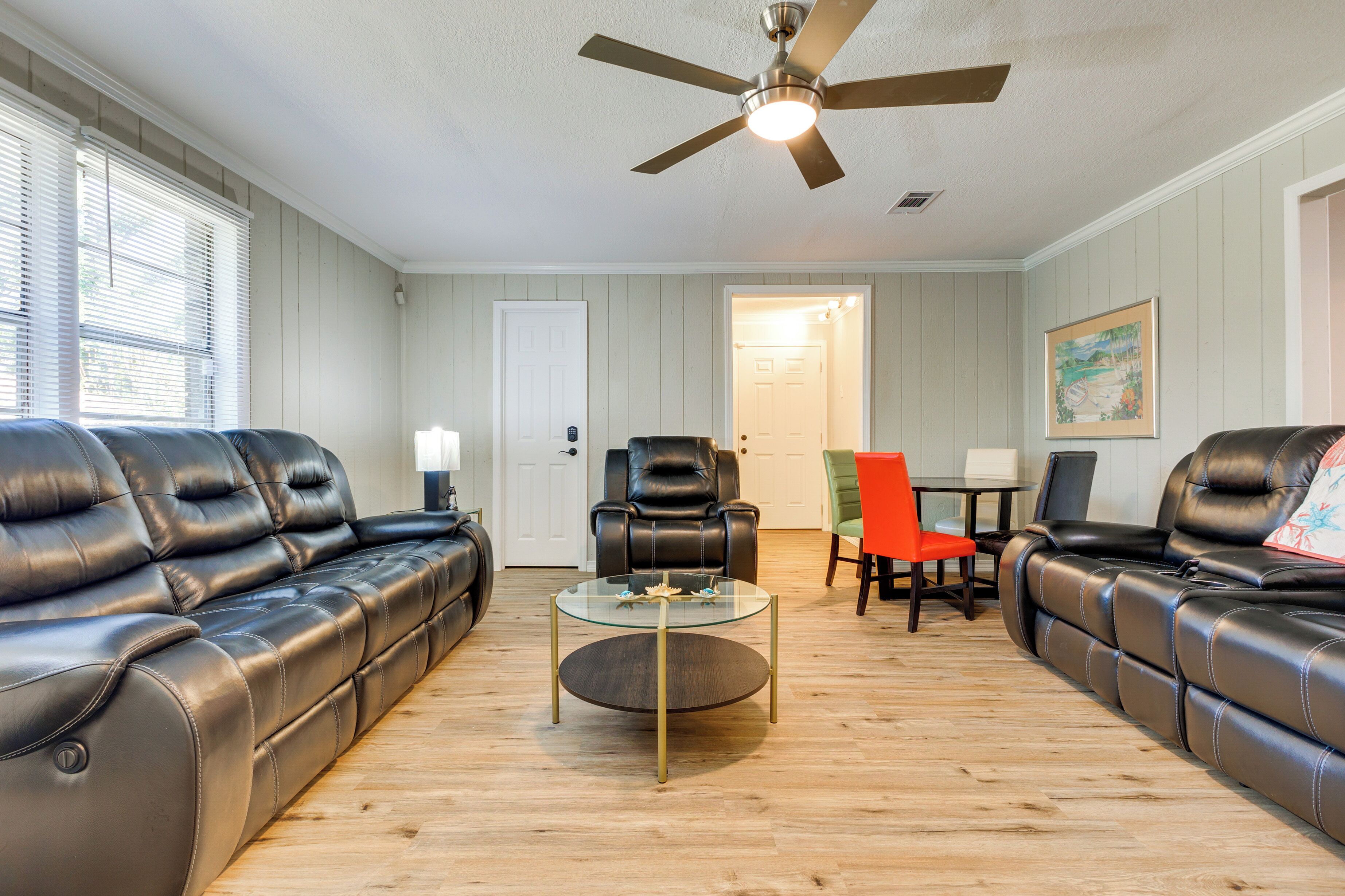 A living room with a sectional sofa, a glass coffee table, a ceiling fan, and a door leading to another room.