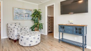 A room with a wooden floor, a blue cabinet with drawers, a television mounted on the wall, and a painting above the cabinet. - Charming Gulfport Home ~ 2 Mi to Marina (Gulfport)