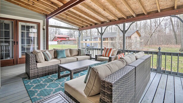 Une terrasse couverte, meublée de meubles en osier, agrémentée d’un tapis à motifs et offrant une vue sur les maisons au loin.