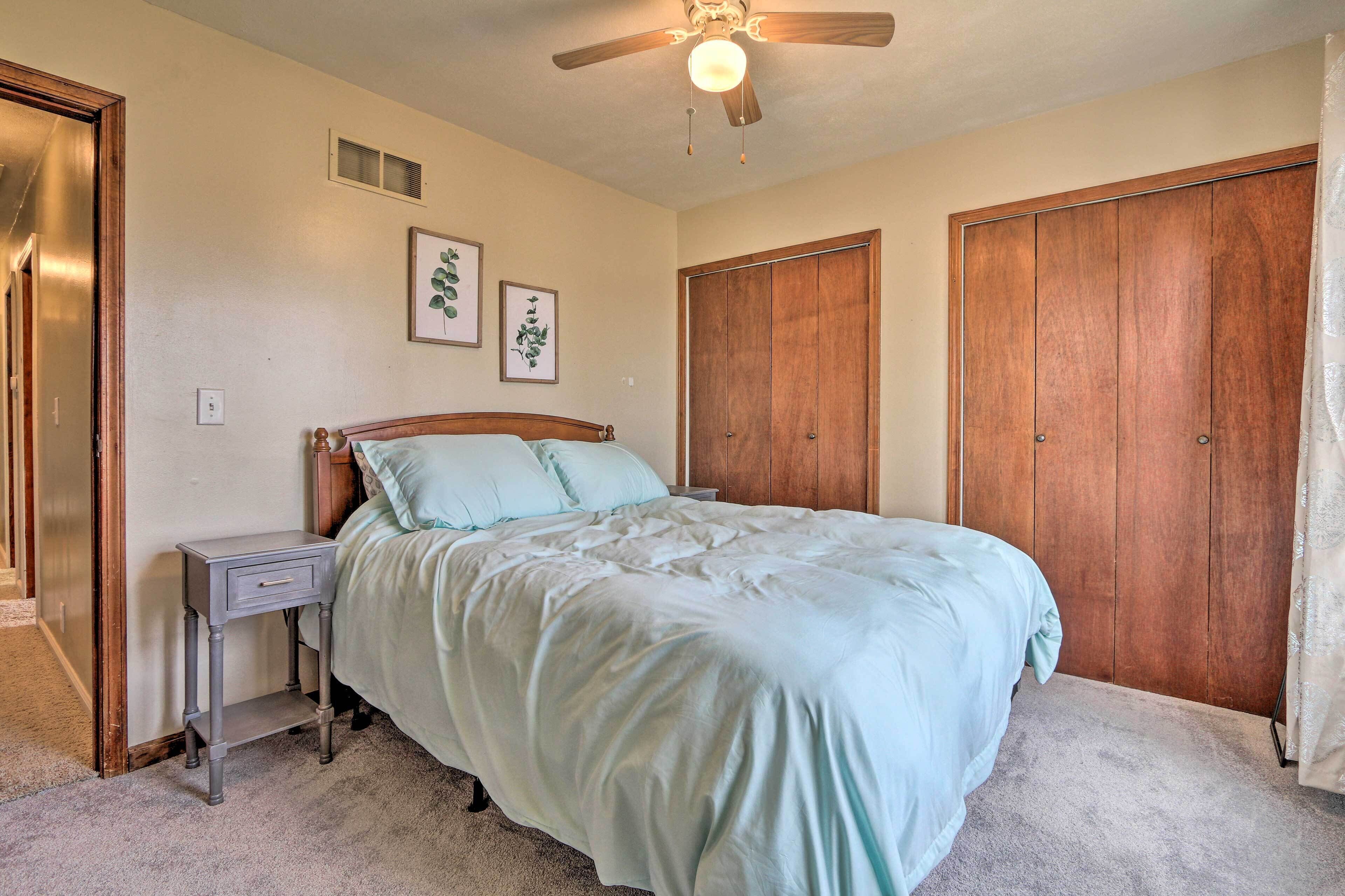 A bedroom with a bed, nightstand, ceiling fan, and wooden wardrobe.