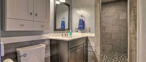 A bathroom with a toilet, sink, mirror, and shower area.