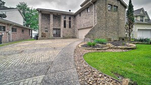 Uma casa residencial com fachada de tijolos, entrada com calçada e jardim da frente ajardinado, com um pequeno jardim e uma árvore.