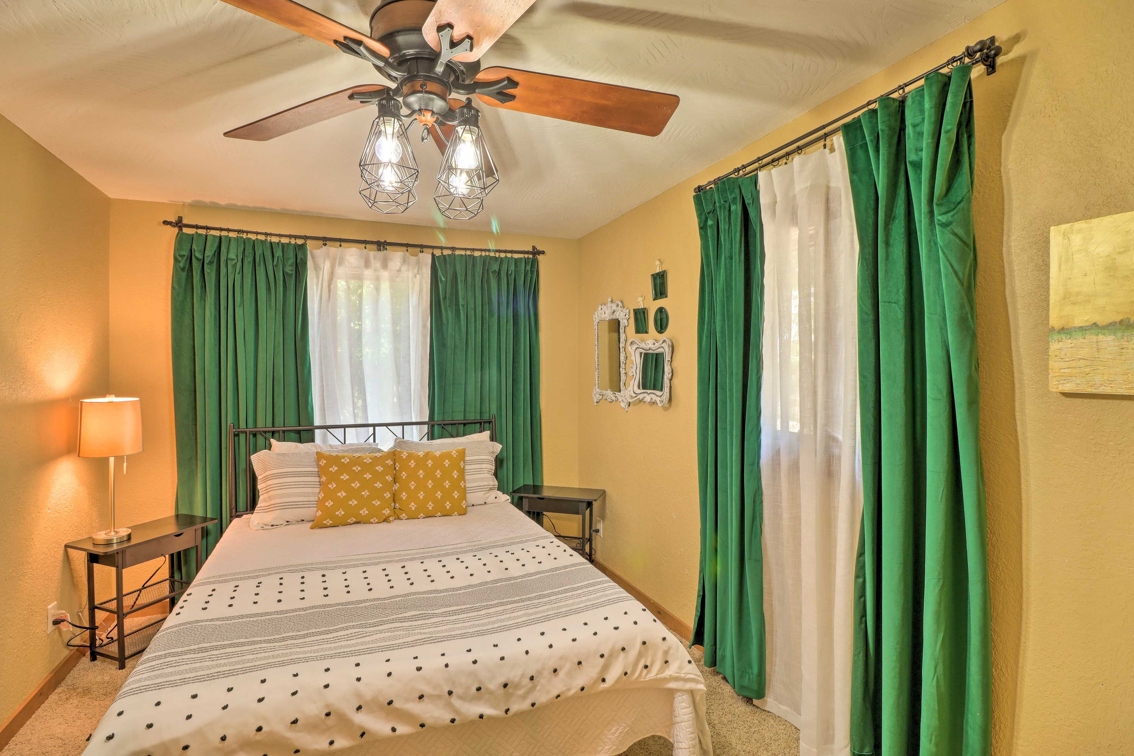A bedroom with a bed, a ceiling fan, a nightstand, a lamp, and green curtains.