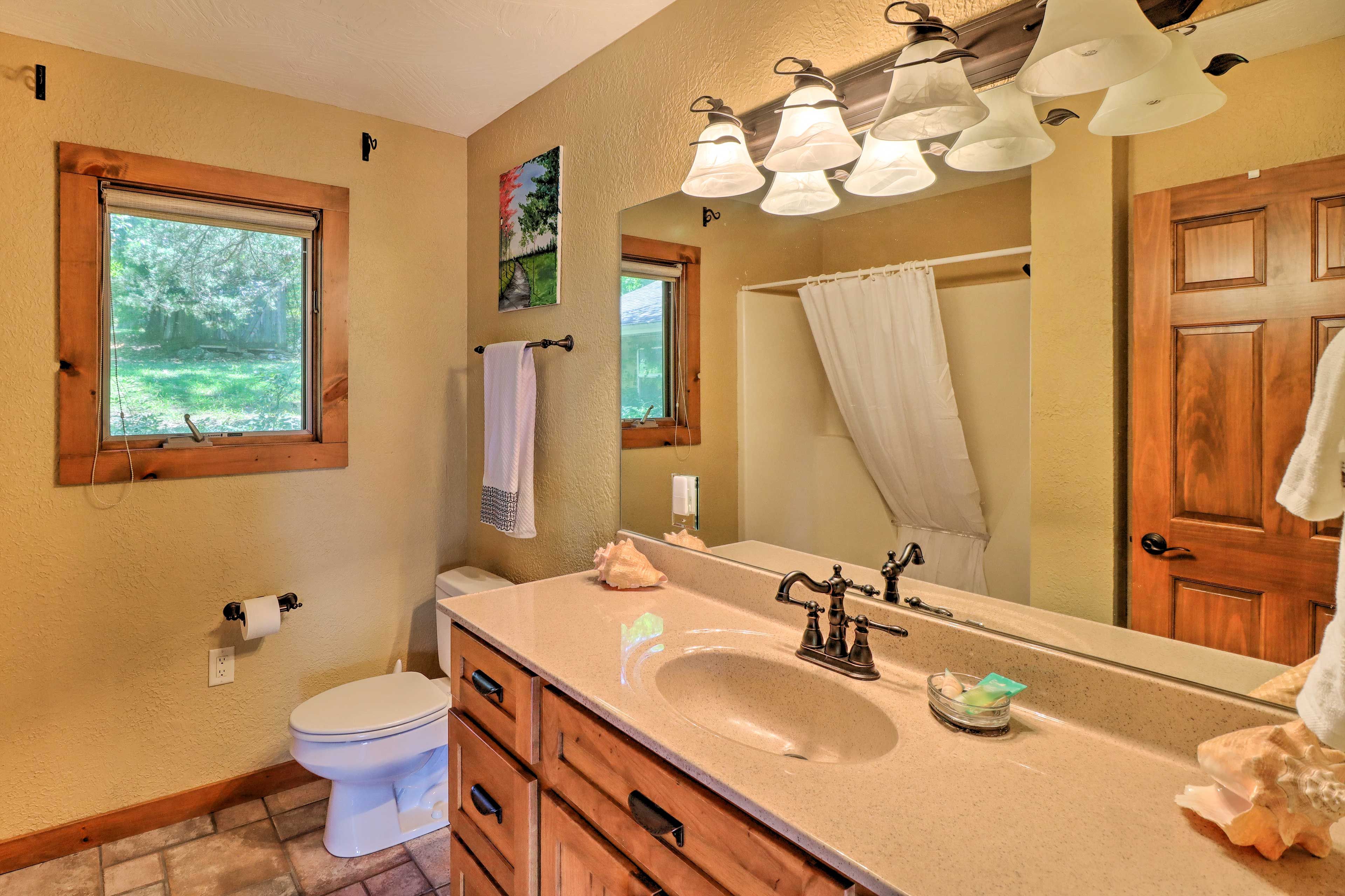 A bathroom with a large mirror, wooden vanity, and a window with a view of trees.