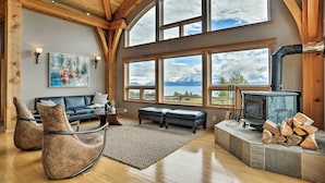 A cozy living room with a fireplace, large windows, a sofa, and a rug. - Home w/ Kachemak Bay View - 5 Miles to Downtown! (Homer)