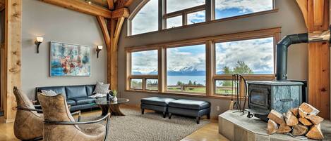 A cozy living room with a fireplace, large windows, a sofa, and a rug.