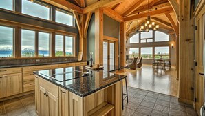A spacious kitchen with large windows, a central island, and a dining area with a view. - Home w/ Kachemak Bay View - 5 Miles to Downtown! (Homer)